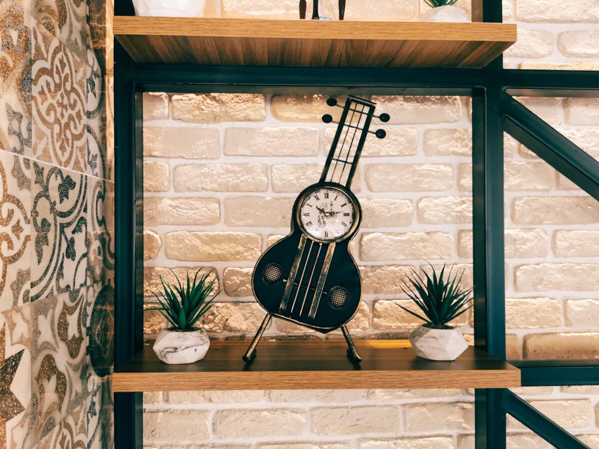 Unique guitar-shaped clock on a decorative brick wall shelf with plants. Perfect for vintage decor.